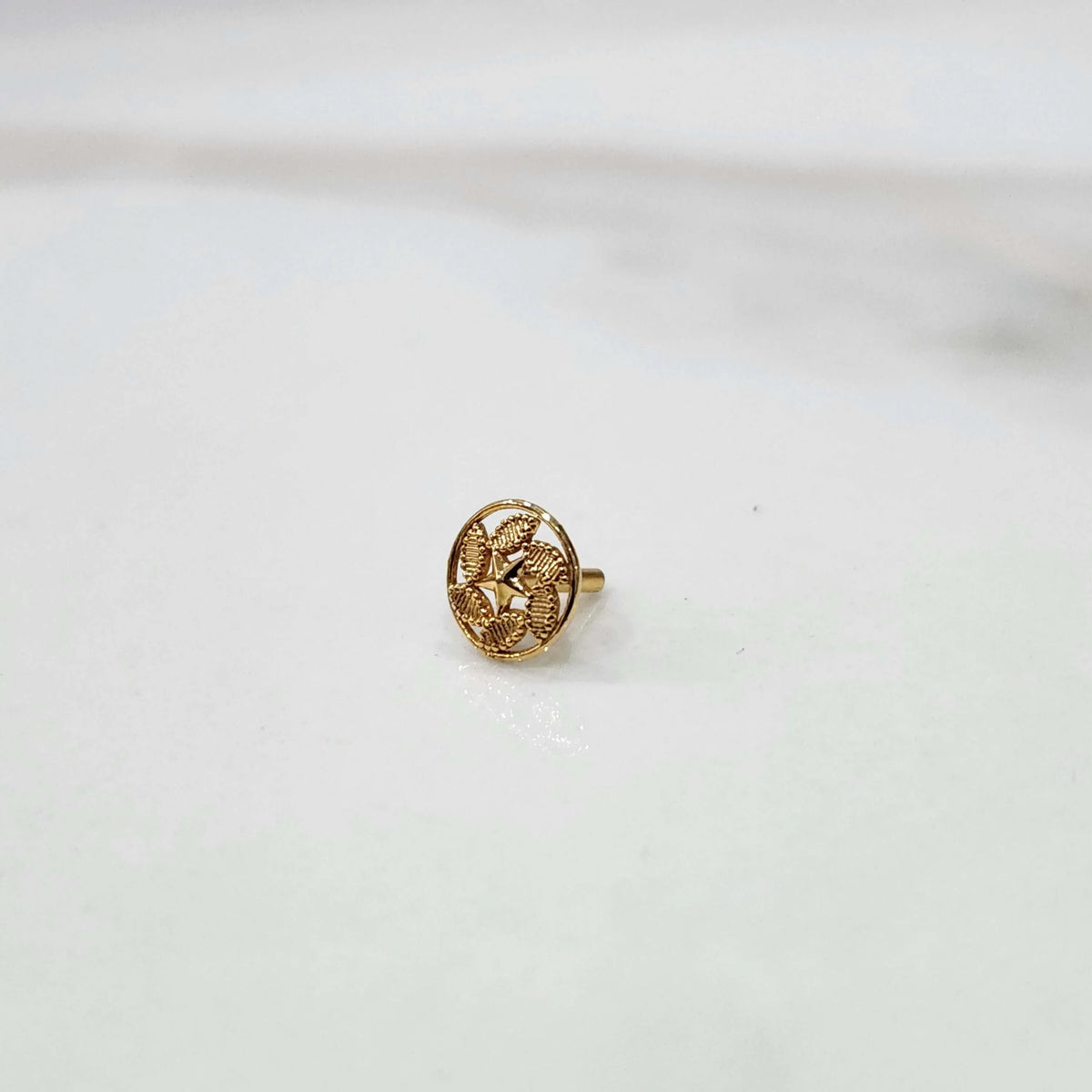 Side view of a small round 18K gold nose pin placed on a white surface showing its post and finish