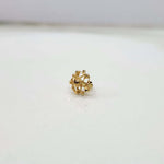 Front view of floral gold nose pin with green and red stone detailing on a white surface