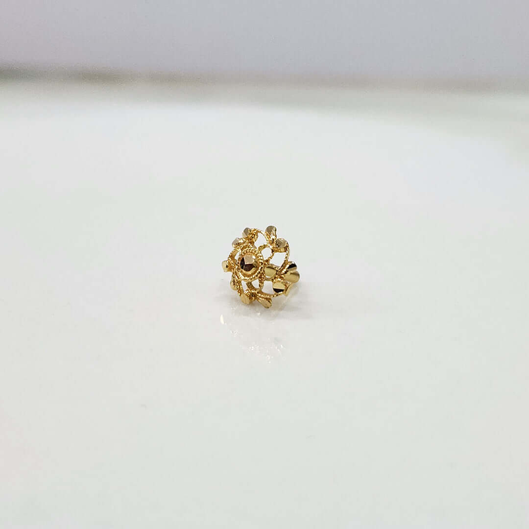 Front view of floral gold nose pin with green and red stone detailing on a white surface