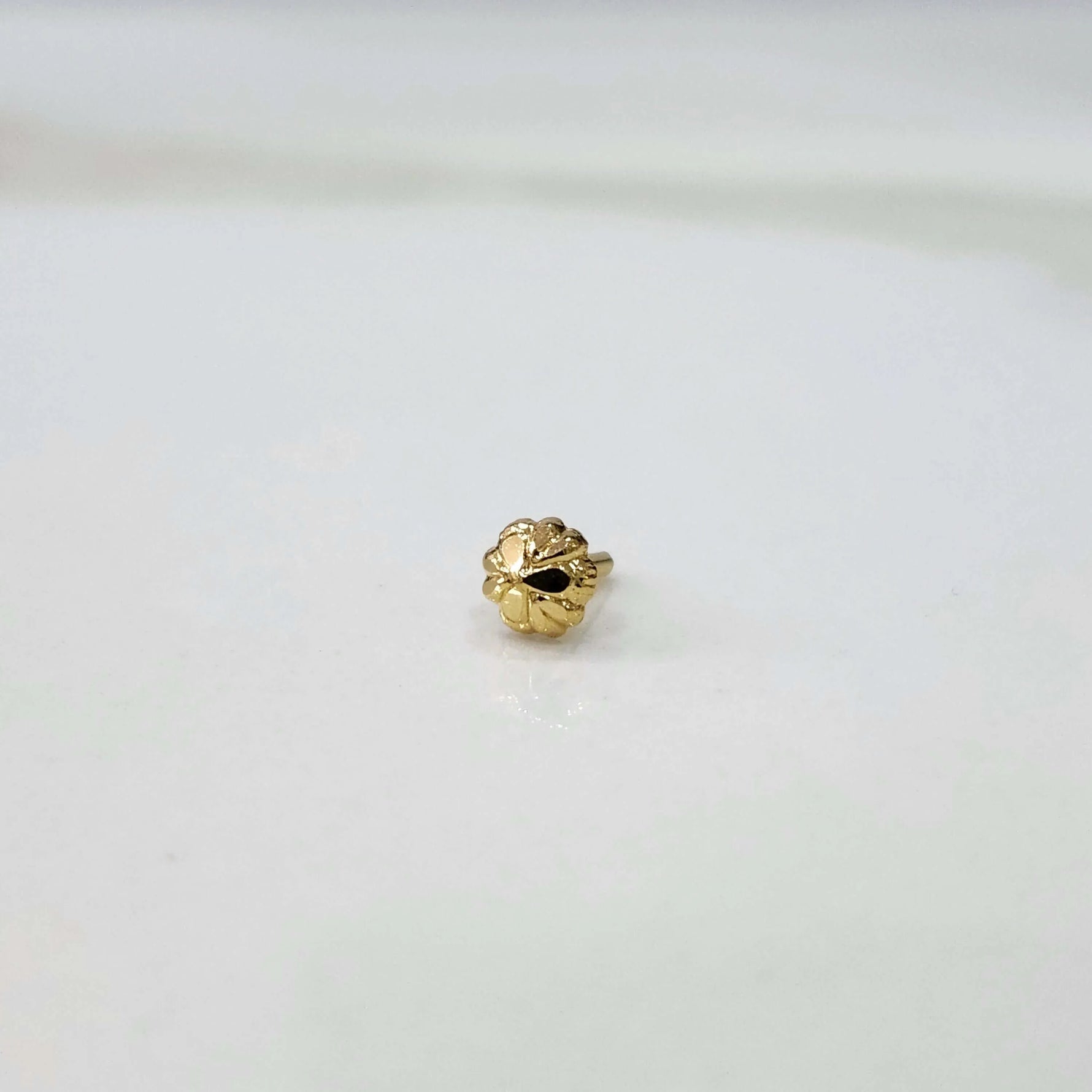 Slight angled view of a delicate gold nose pin placed on a white surface showing its lightweight everyday design