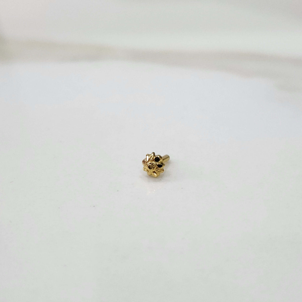 Slight angled view of a tiny gold nose pin on a white surface highlighting its fine detailing and subtle shine
