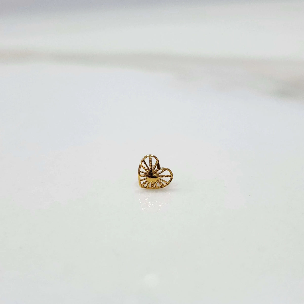 Side view of a delicate 18K nose pin gold on a white surface highlighting lightweight design and smooth finish