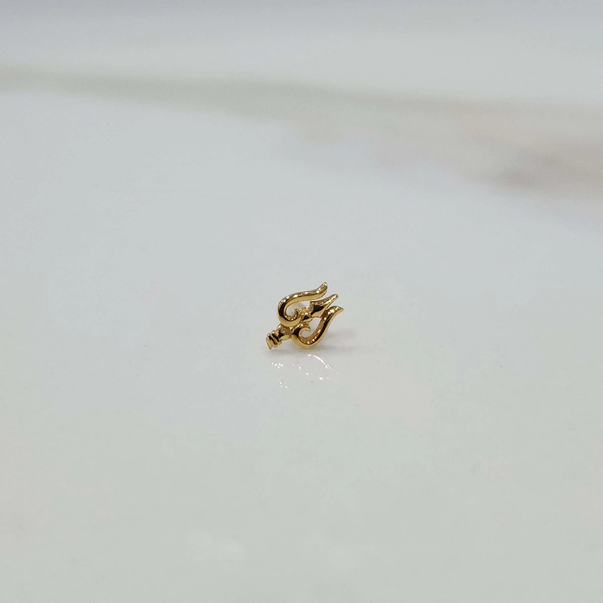 Close-up of tiny gold nose pin on white marble surface showing intricate detailing