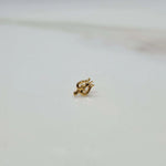 Close-up of tiny gold nose pin on white marble surface showing intricate detailing