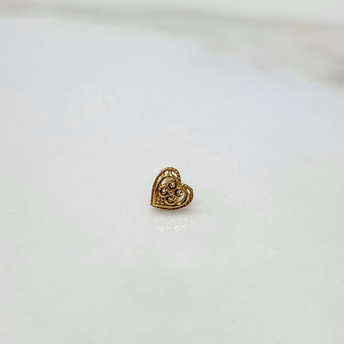 Front view of a small heart design gold nose pin placed on a white background showing compact size