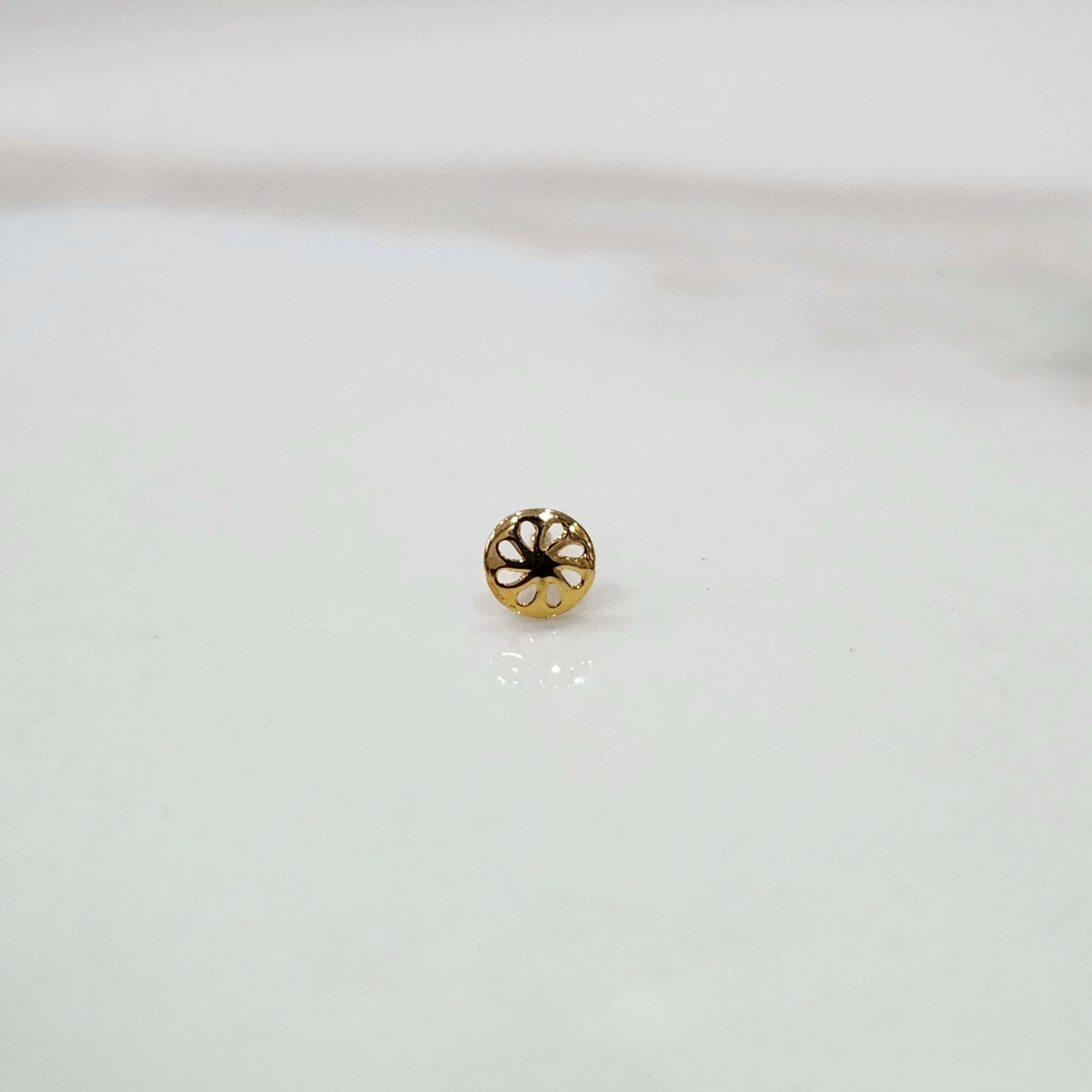 Front view of a small gold nose pin placed on a white background showing its compact floral detailing
