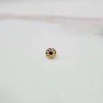 Front view of a small gold nose pin placed on a white background showing its compact floral detailing