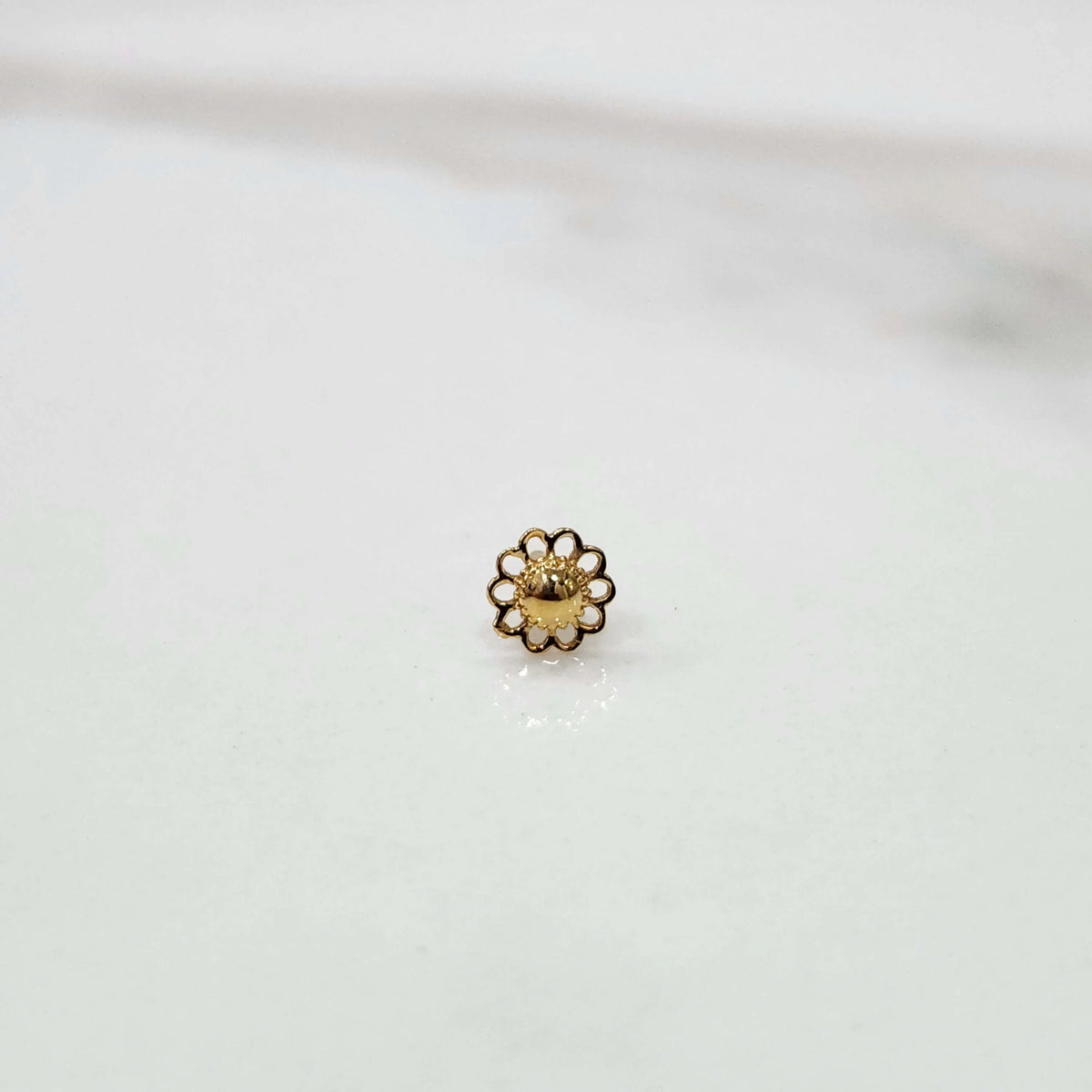 Front view of a tiny 18K gold nose pin placed on a white surface showing its compact size and fine craftsmanship