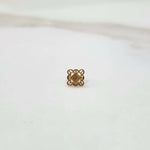 Front view of a small geometric 18K gold nose pin placed on a white surface showing its precise design