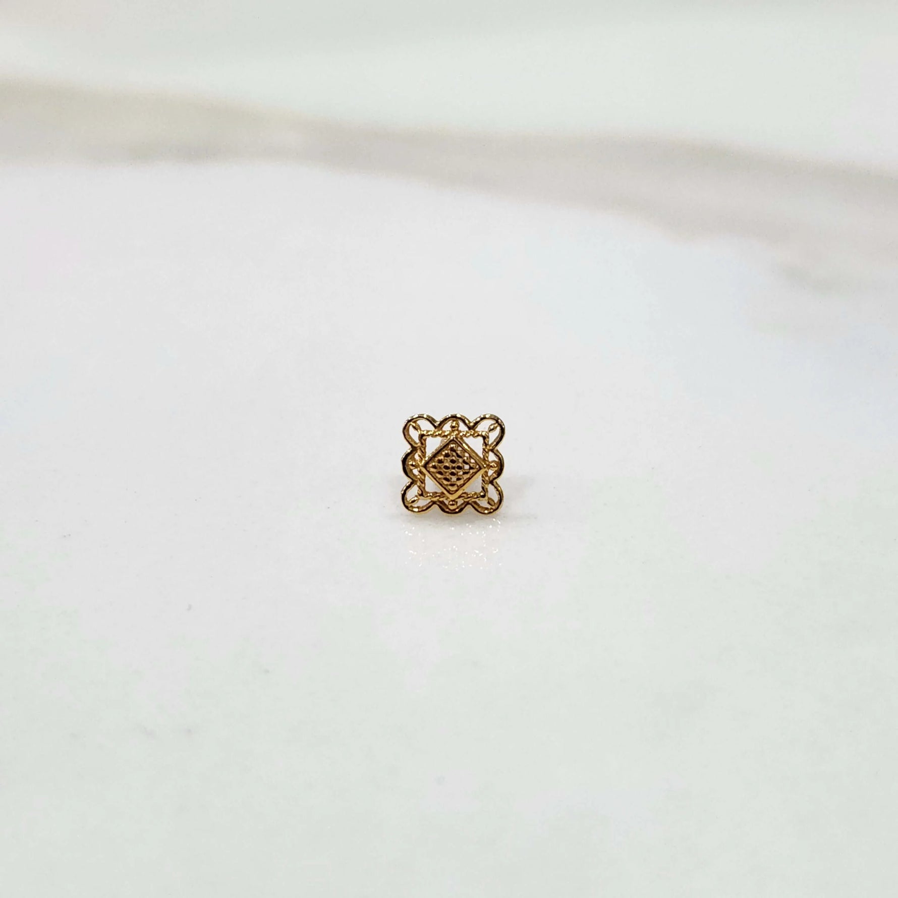 Front view of a small geometric 18K gold nose pin placed on a white surface showing its precise design