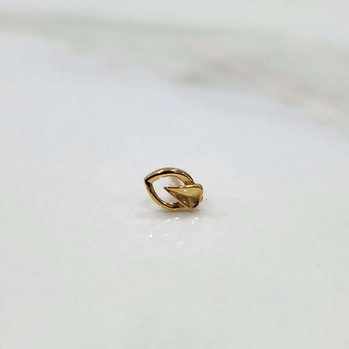 Close up of a small 18K gold nose pin placed on a white background showing fine detailing