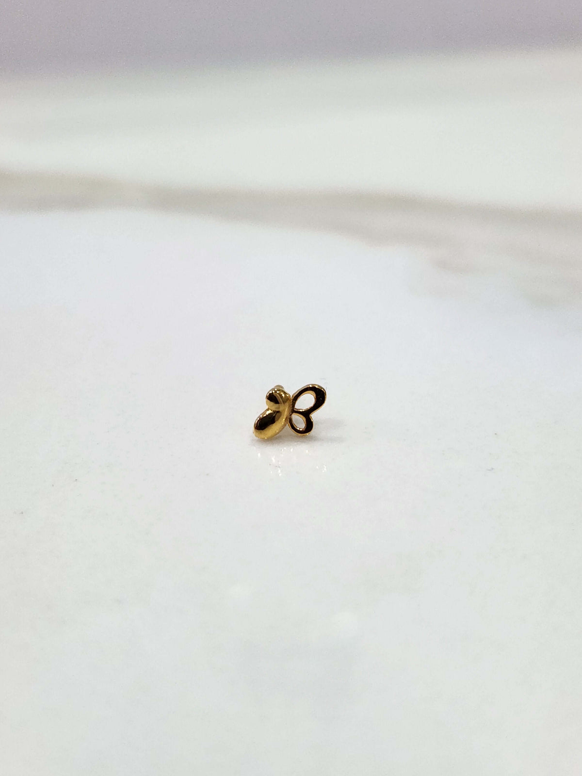 Distant front view of a tiny floral 18K nose pin gold on a white background showing its minimal size and subtle shine