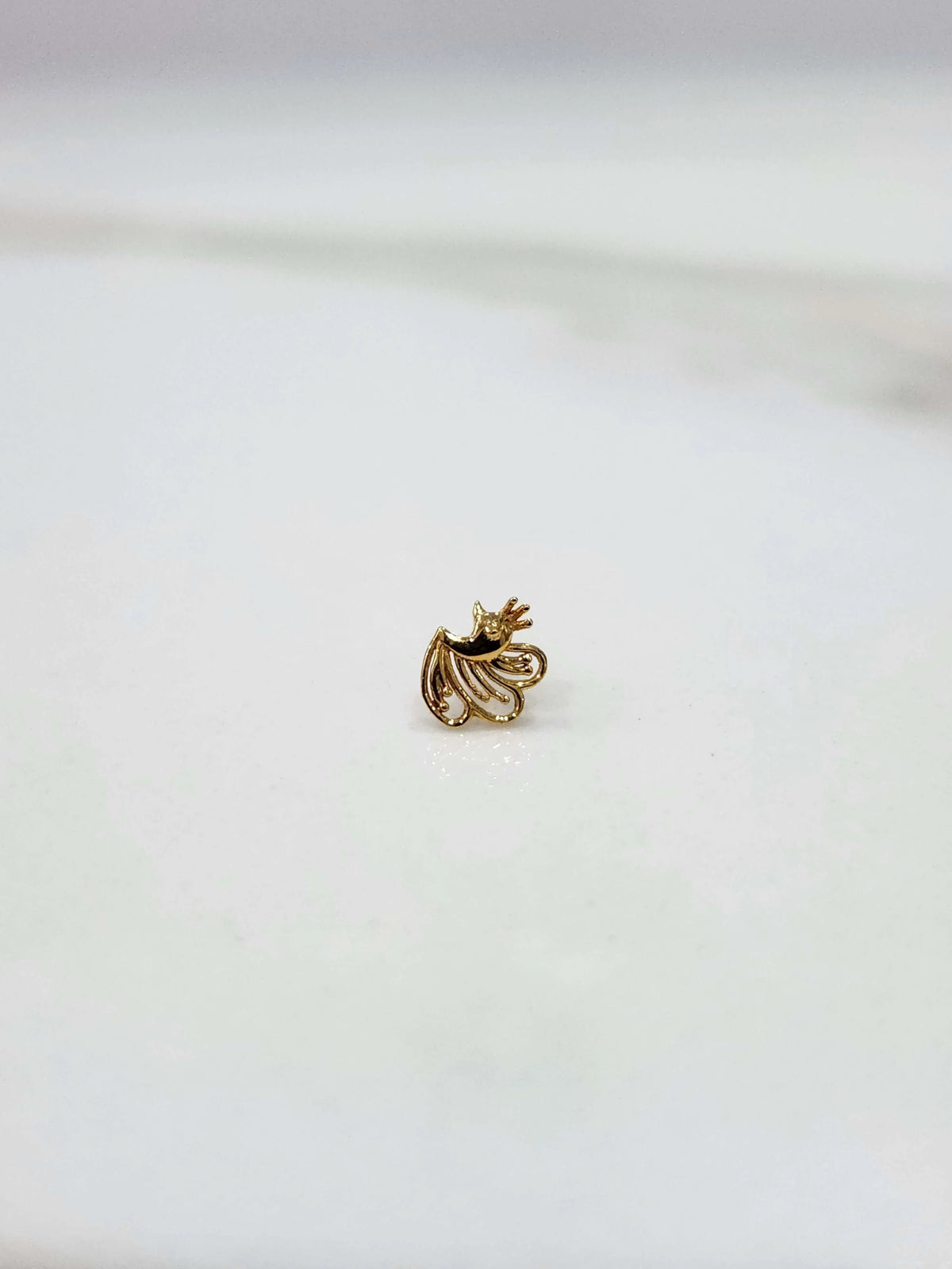 Side view of a small 18K nose pin gold placed on a white surface showing fine detailing and lightweight finish