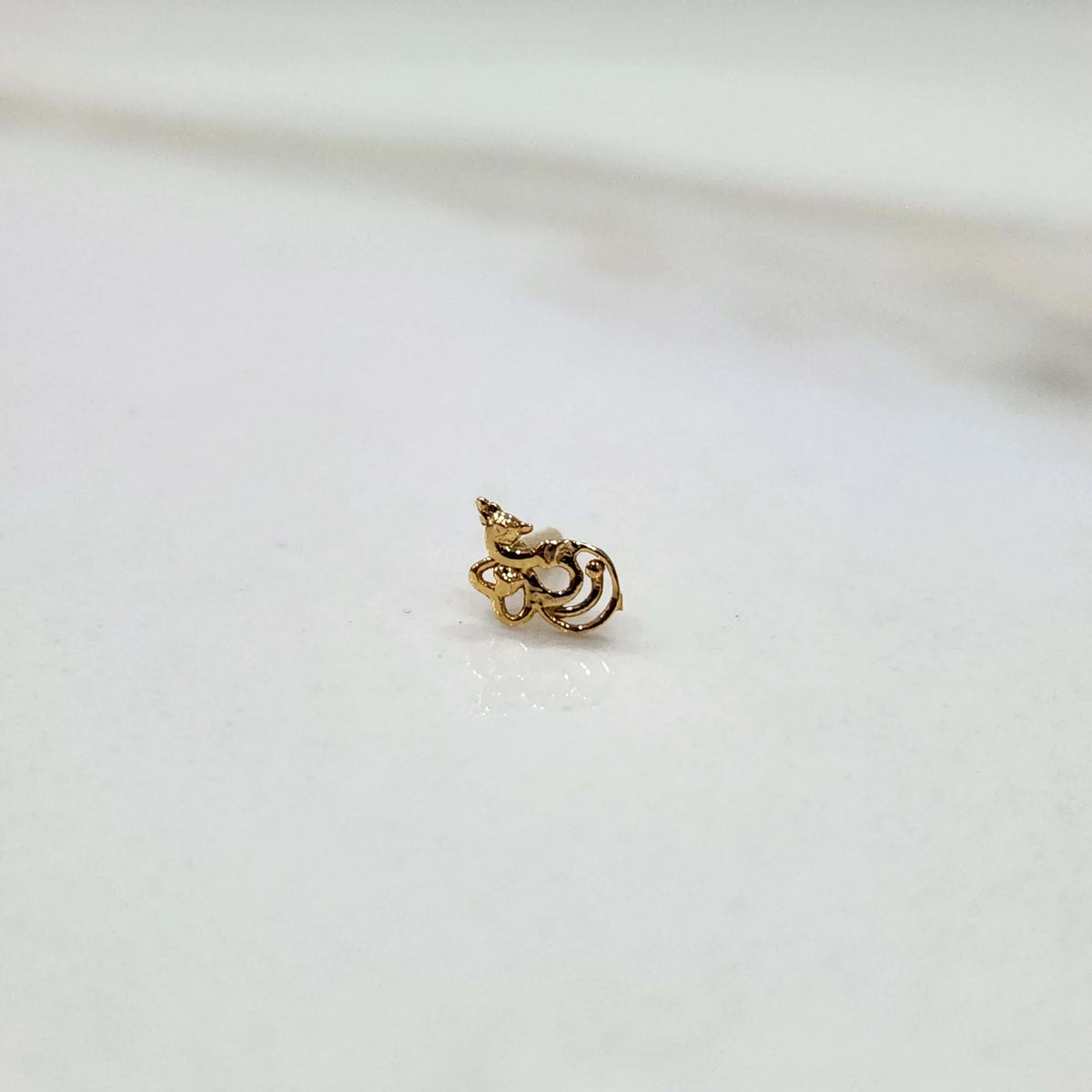 Side view of a delicate 18K nose pin gold on a white background highlighting its curved design and polished finish