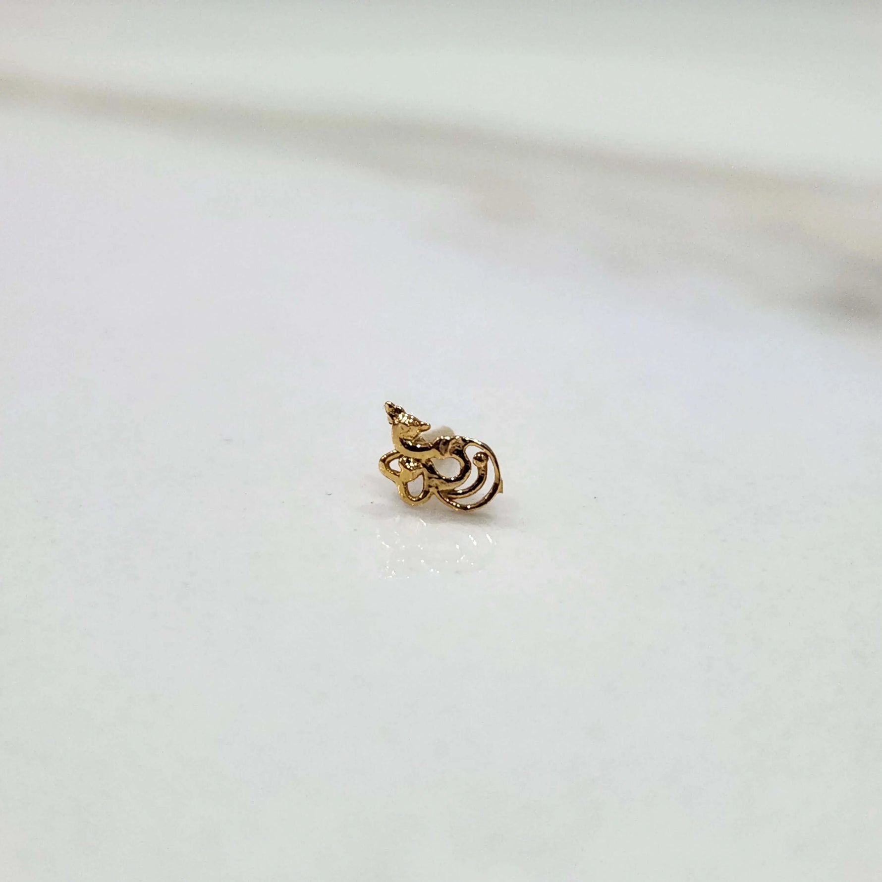 Side view of a delicate 18K nose pin gold on a white background highlighting its curved design and polished finish