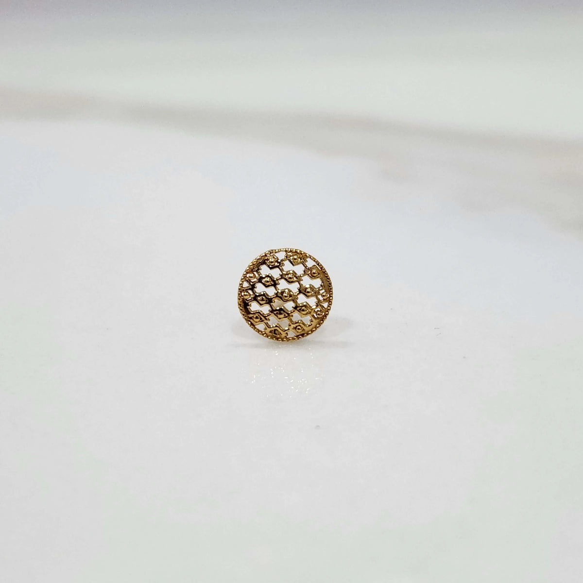 Close-up of round textured 18K gold nose pin on a smooth white background showing its polished finish