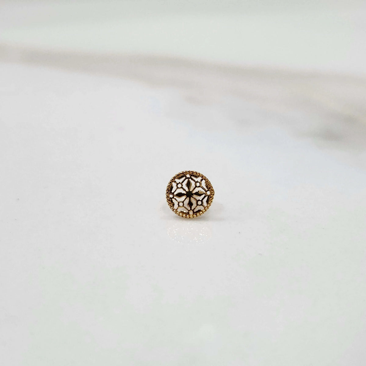 Front view of a small round 18K nose pin gold placed on a white surface highlighting its compact detailing