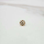 Slight angled view of a textured circular 18K gold nose pin on a white surface highlighting its polished finish and craftsmanship