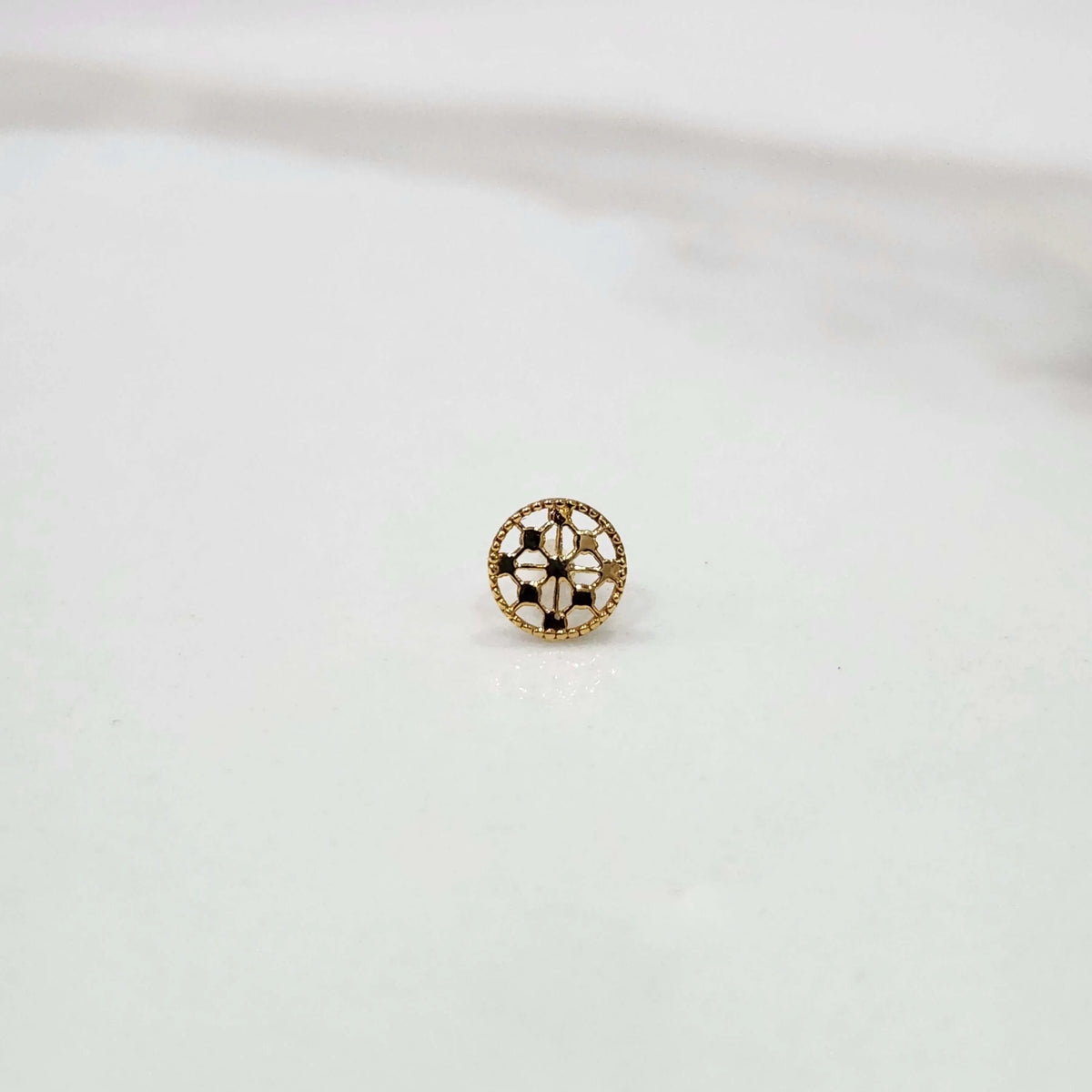 Slight angled view of a textured circular 18K gold nose pin on a white surface highlighting its polished finish and craftsmanship