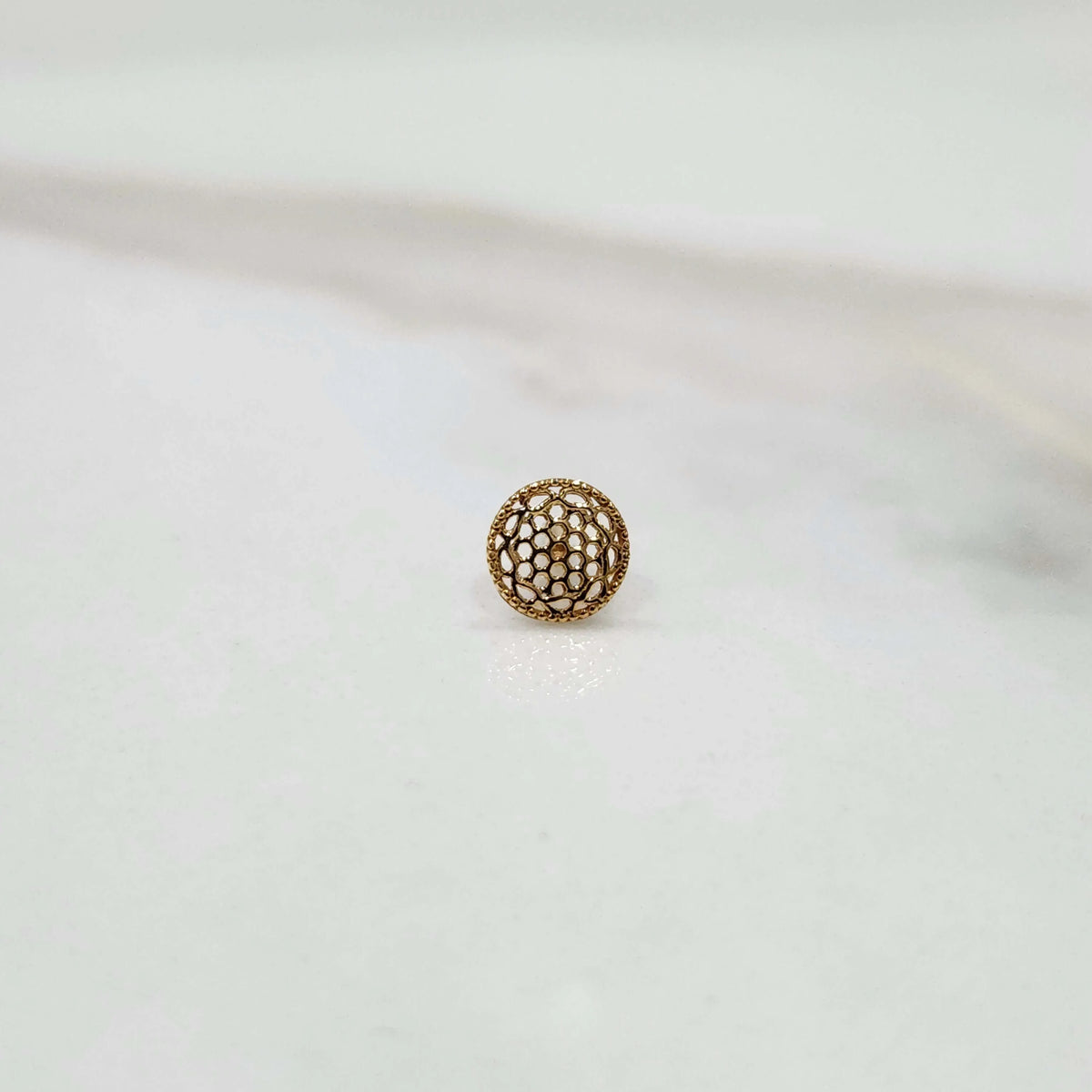 Side view of a tiny round 18K nose pin gold on a white background showing its compact size and subtle shine