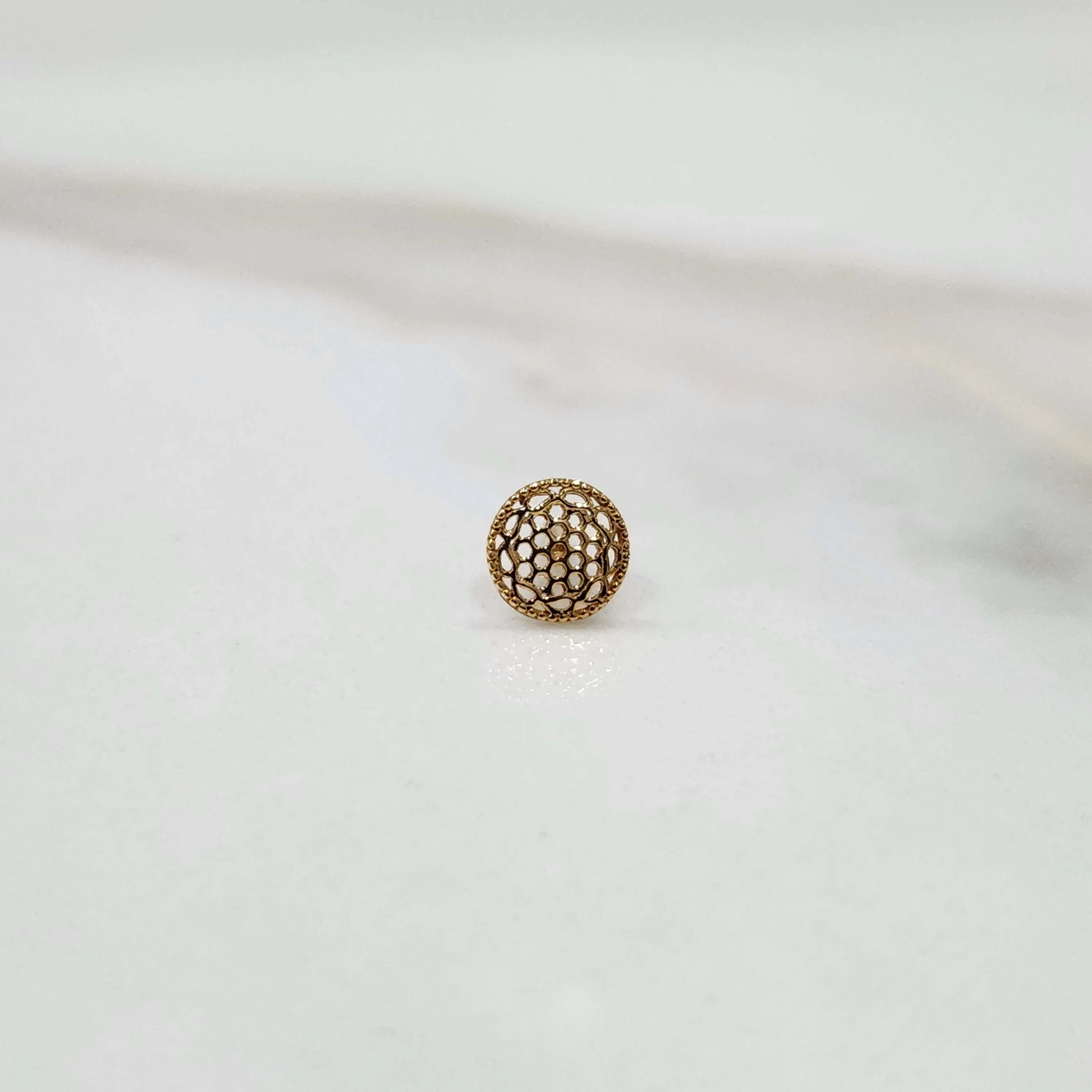 Side view of a tiny round 18K nose pin gold on a white background showing its compact size and subtle shine