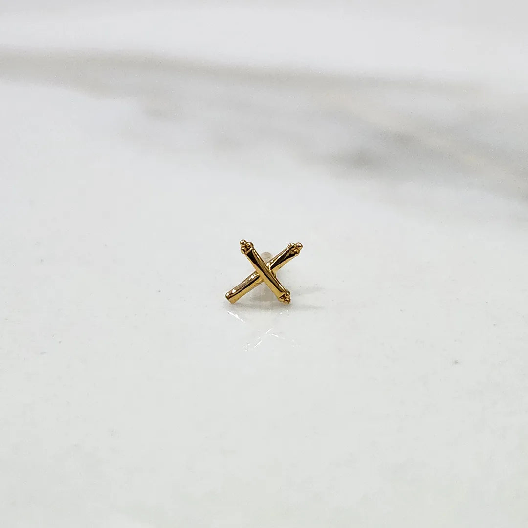 Tiny cross gold nose pin placed on a white surface showing delicate craftsmanship