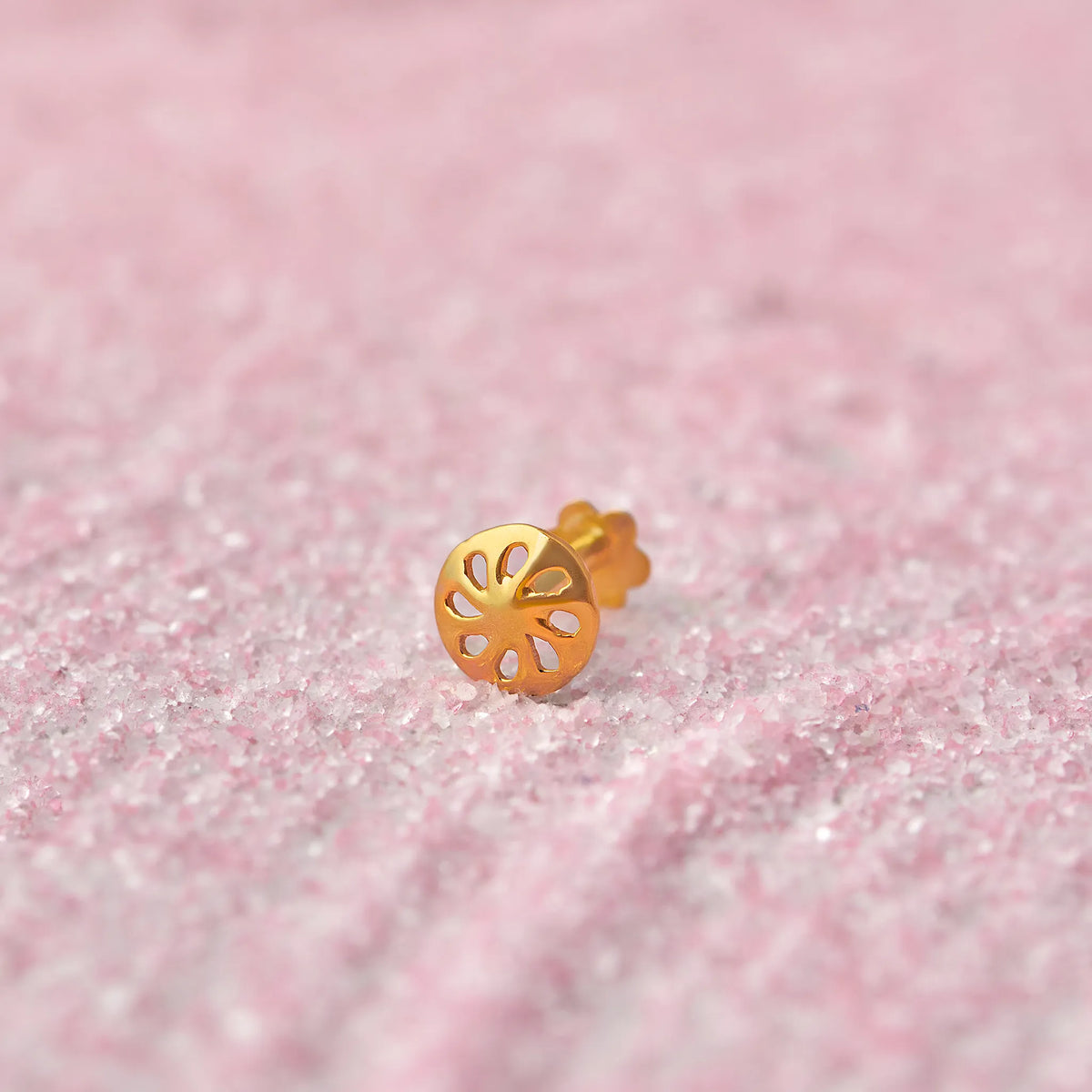 Close up of a floral cutwork gold nose pin placed on a soft pink textured surface highlighting its delicate open design