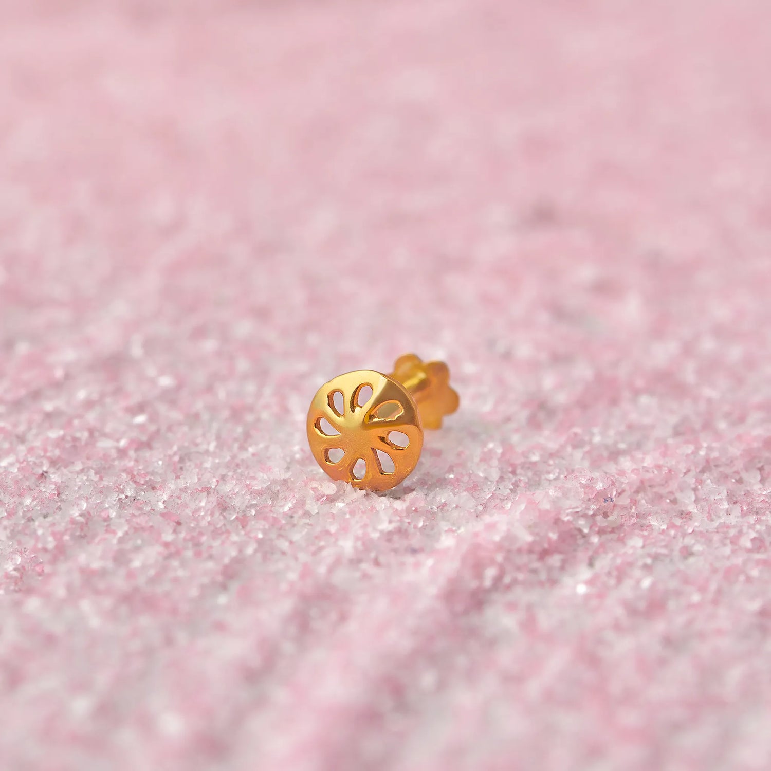Close up of a floral cutwork gold nose pin placed on a soft pink textured surface highlighting its delicate open design