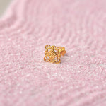 Close up of an intricate geometric design 18K gold nose pin placed on a soft pink textured background highlighting fine craftsmanship