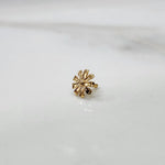 Top view of daisy shaped gold nose pin on a white surface showing symmetrical petal detailing
