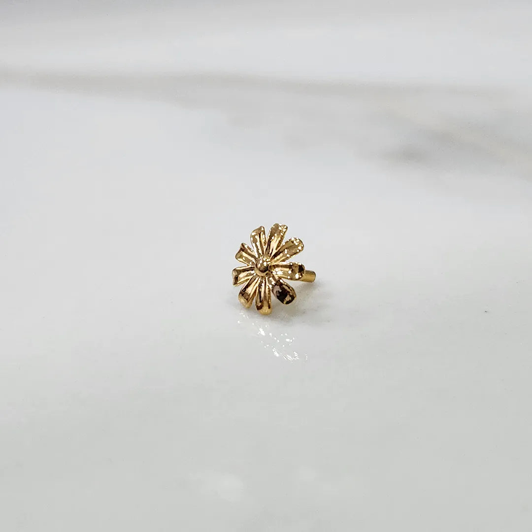 Top view of daisy shaped gold nose pin on a white surface showing symmetrical petal detailing