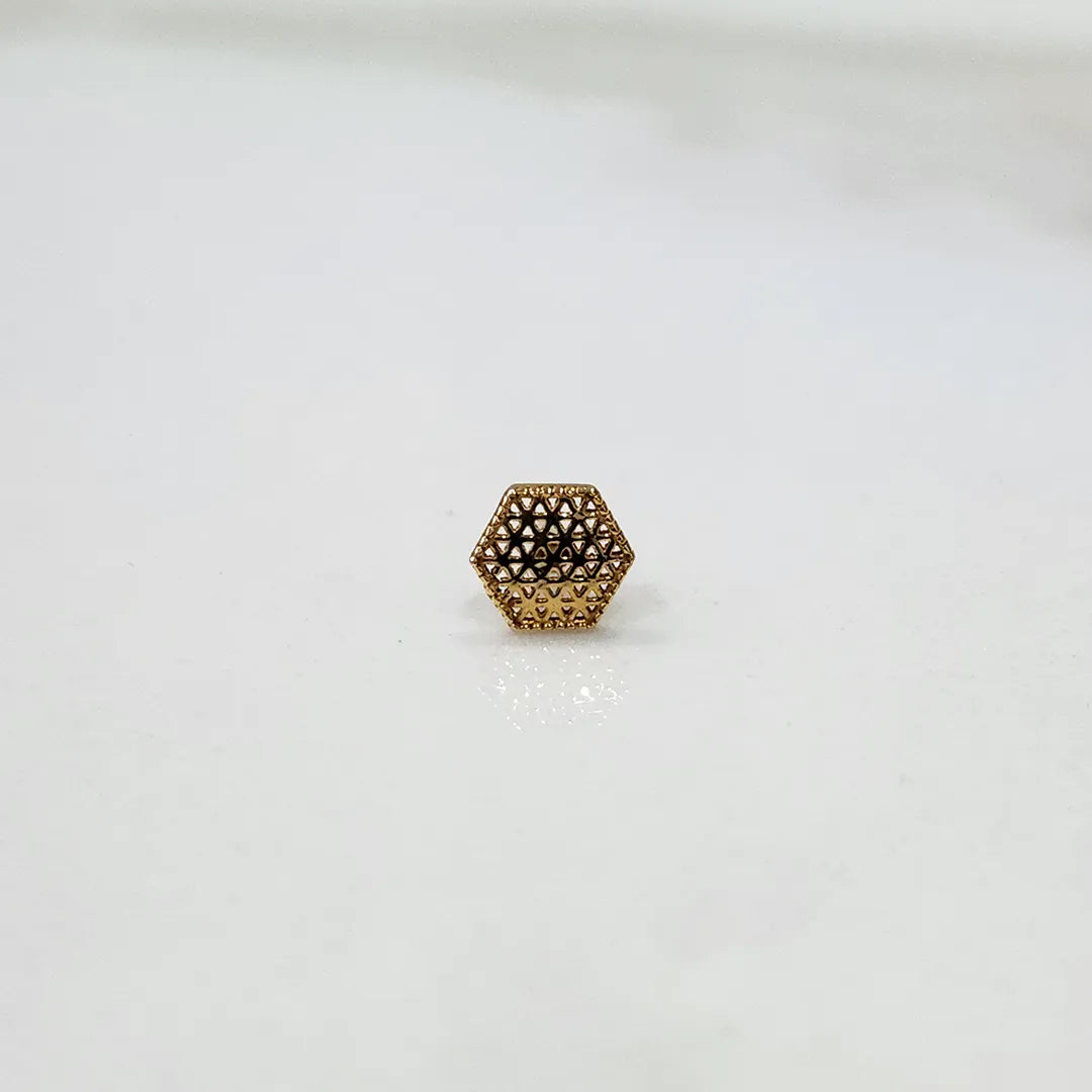 Front view of small hexagonal lattice gold nose pin placed on a white surface highlighting compact design