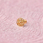 Close up of a round patterned 18K gold nose pin placed on a soft pink textured background highlighting detailed craftsmanship