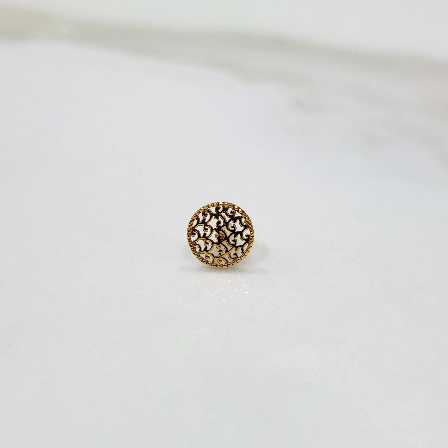 Side angled view of a round gold nose pin on a white surface showing its compact size and finish