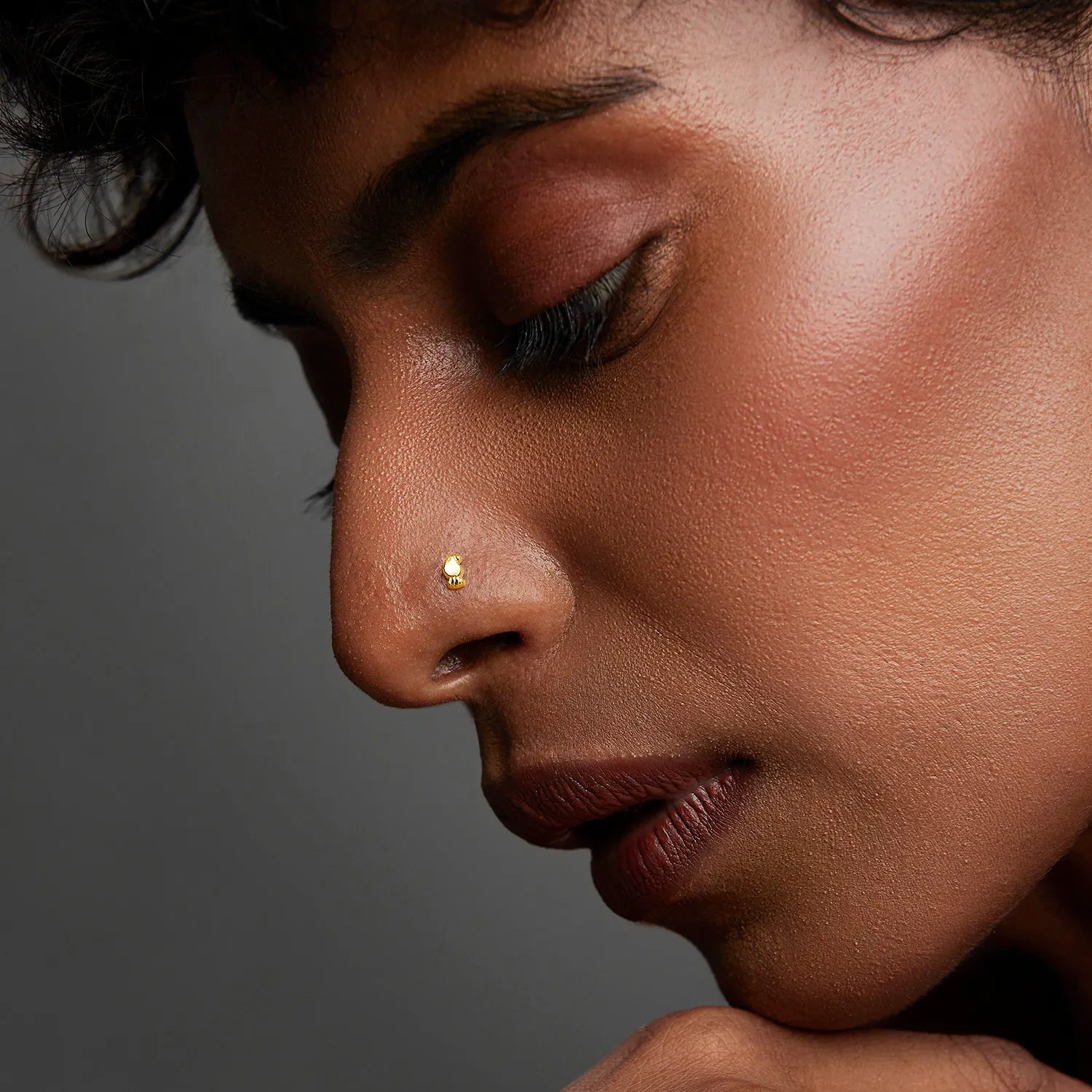 Woman wearing a minimalist gold nose pin in a soft side profile showing an elegant and subtle look