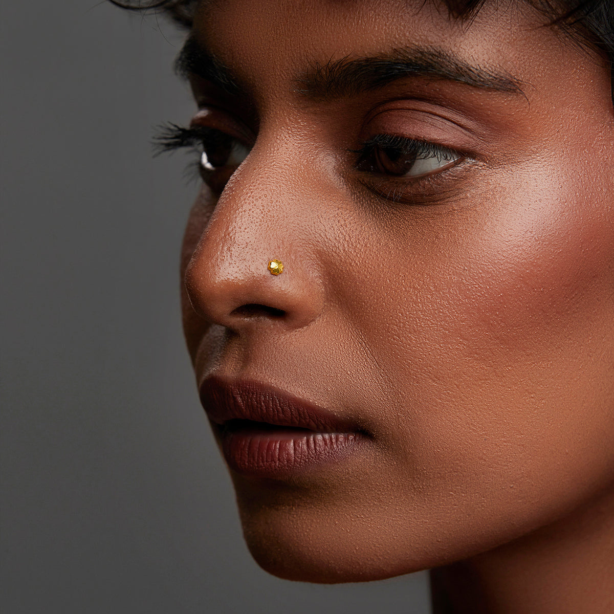 Side profile of a woman wearing a delicate gold nose pin showcasing a minimal everyday look