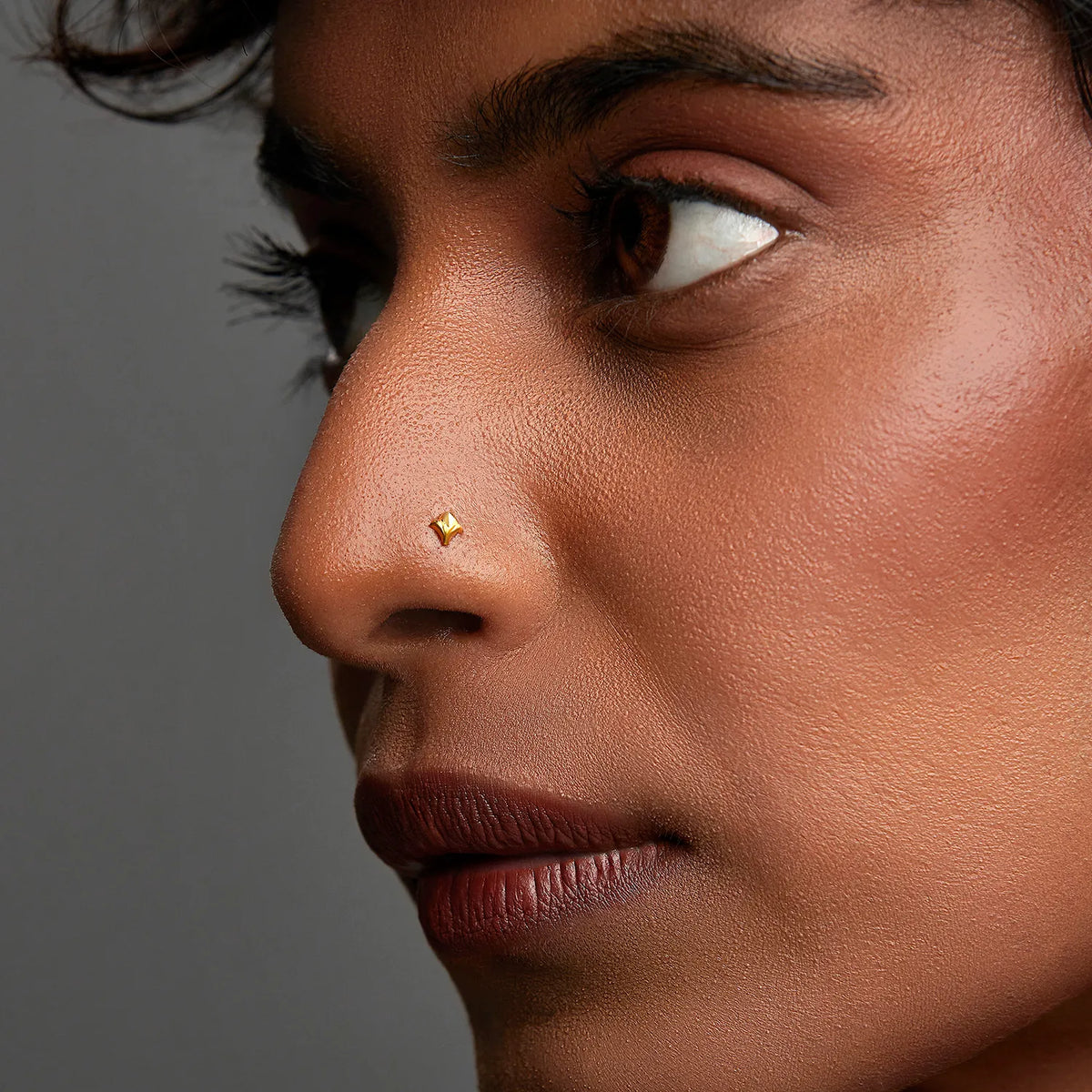 Woman wearing a tiny 18K gold nose pin shown in side profile for a subtle everyday look