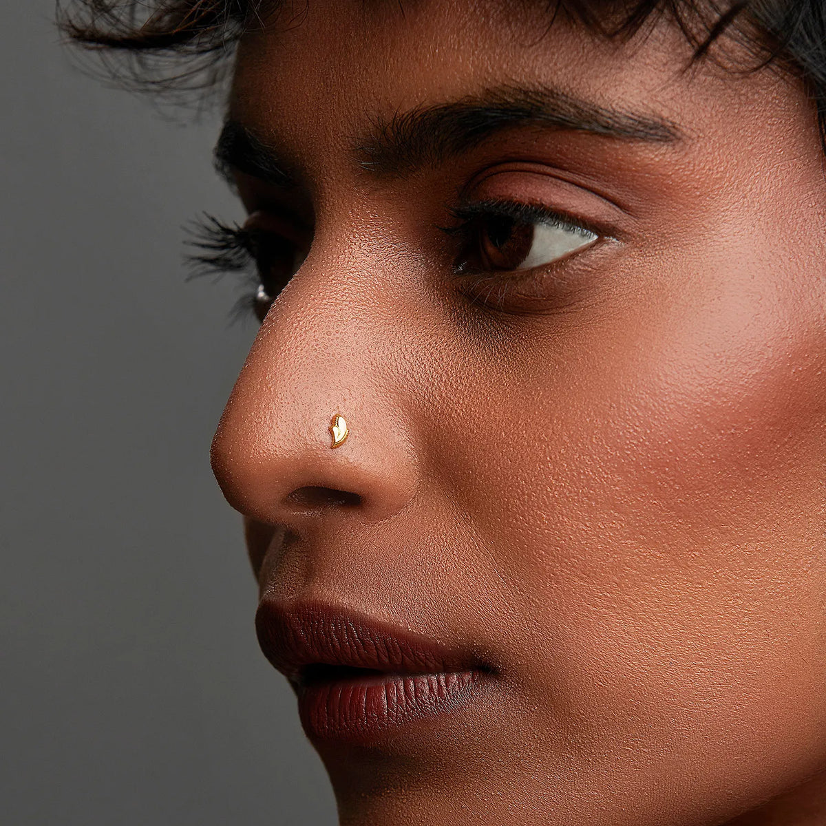 Woman wearing a delicate gold nose pin shown in side profile highlighting an elegant everyday look