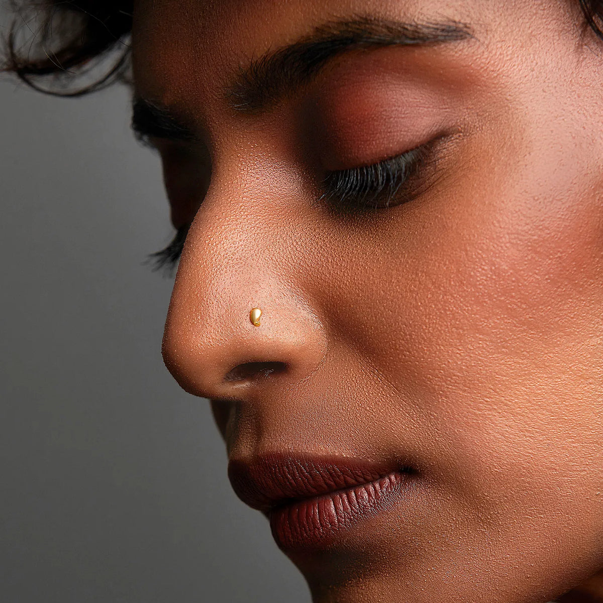 Woman wearing a delicate 18K gold nose pin shown in side profile highlighting a refined everyday look