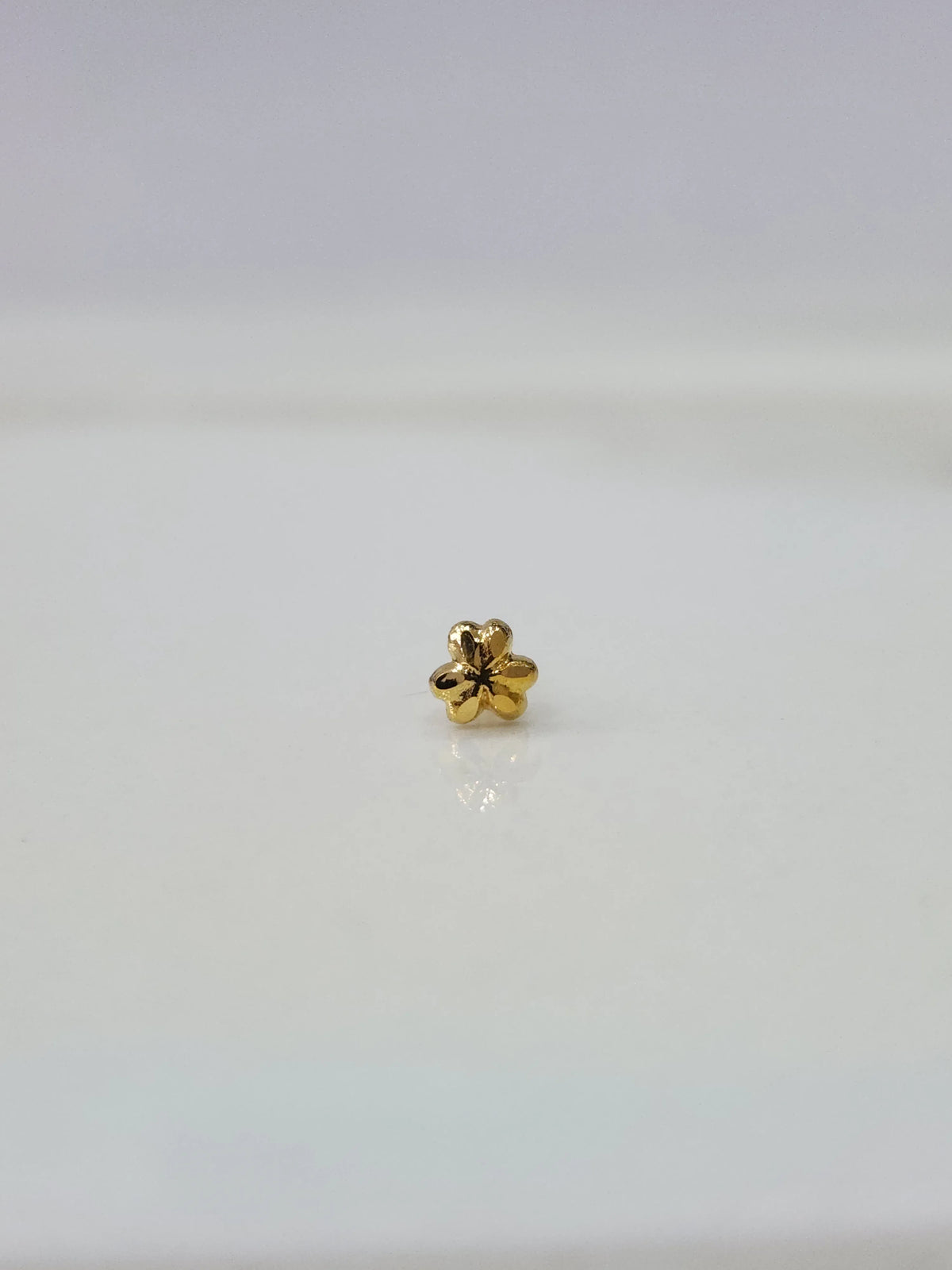Front view of tiny floral 18K gold nose pin on a white background showing delicate craftsmanship