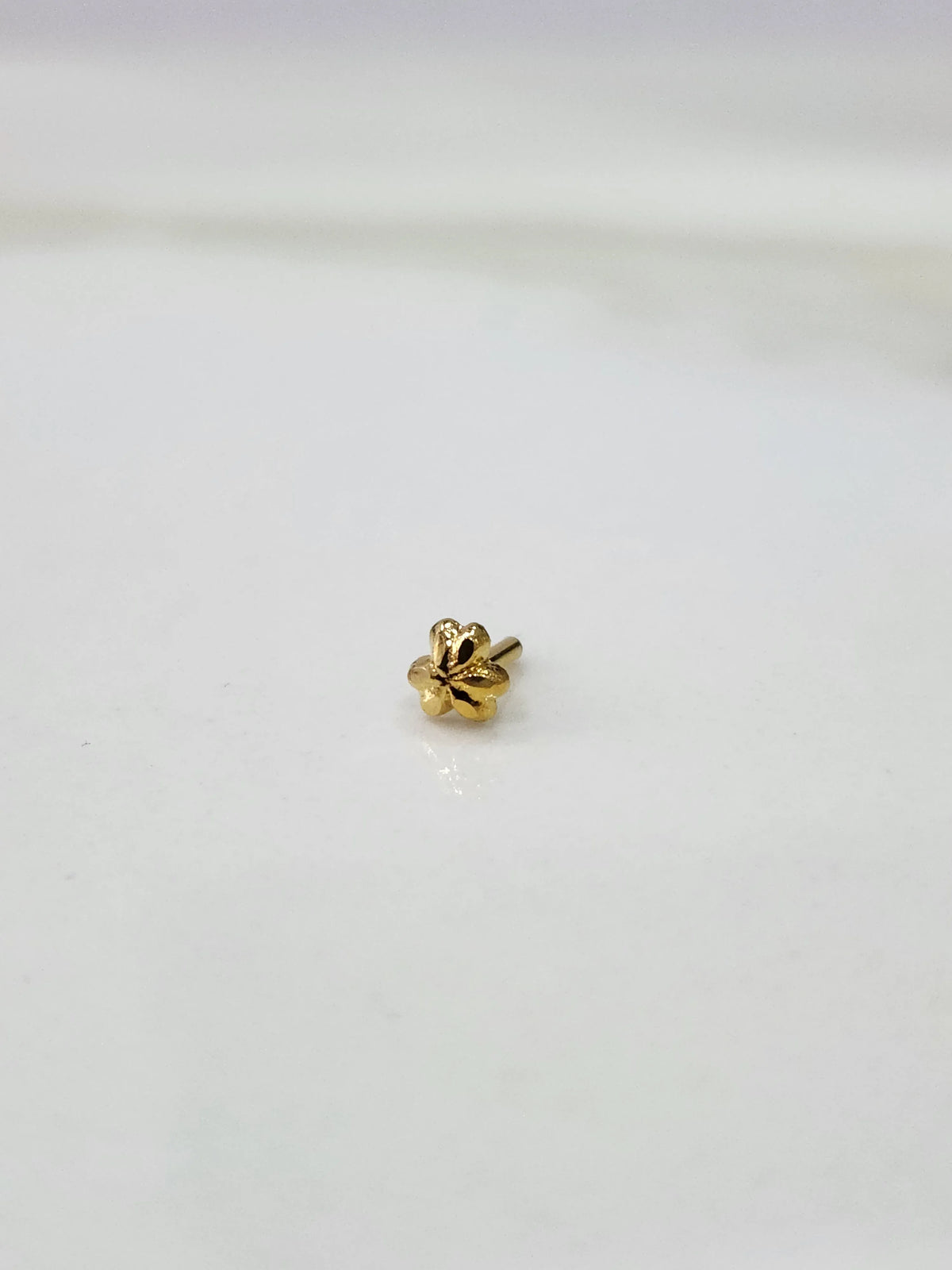 Side angle view of floral 18K gold nose pin on a white surface highlighting its compact and lightweight design