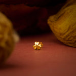 Close up of small floral 18K gold nose pin placed on a warm terracotta surface highlighting its polished finish