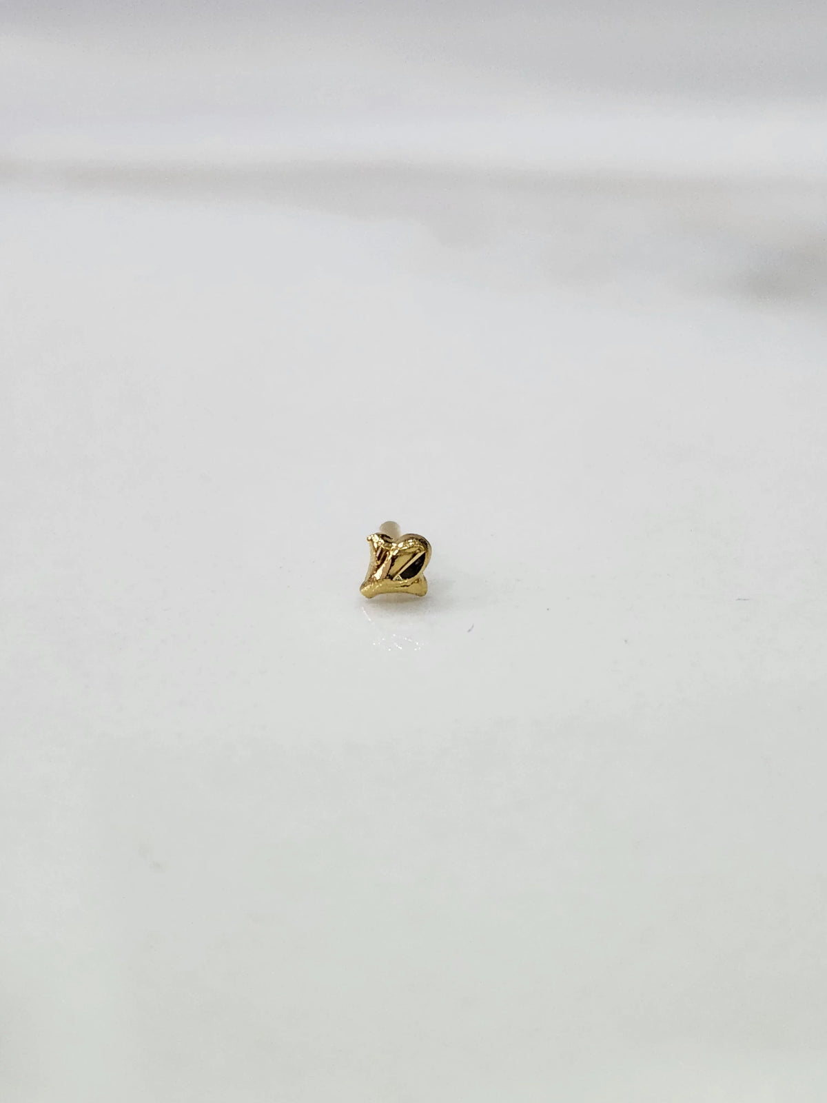 Side view of lightweight 18K gold nose pin on a white surface highlighting compact design and fine detailing