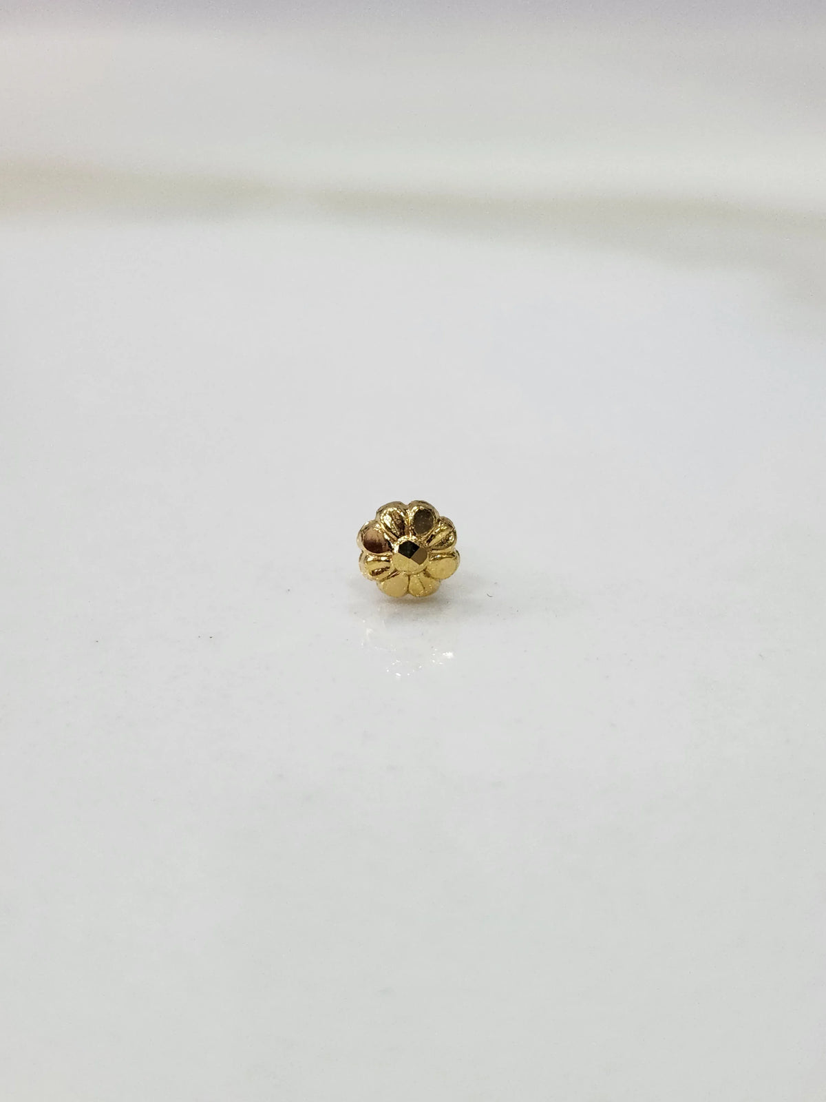 Small gold nose pin photographed on a smooth white surface highlighting its delicate design