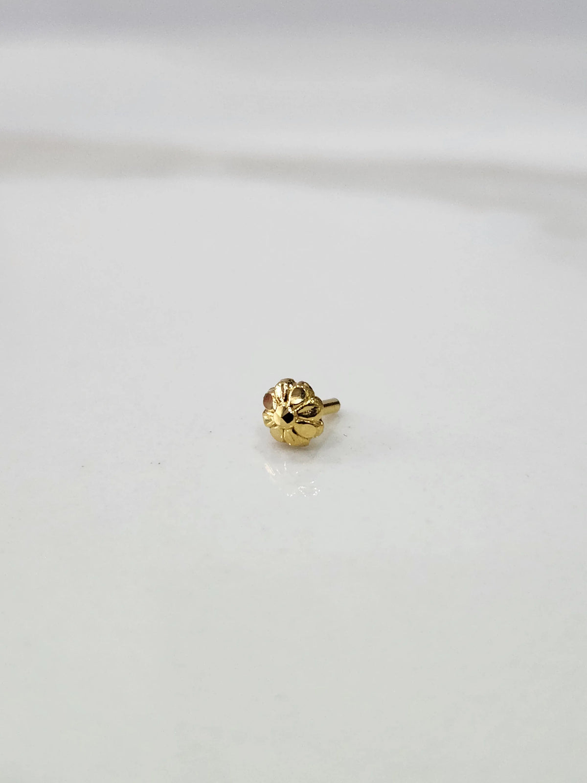 Close-up of a tiny gold nose pin placed on a white marble surface