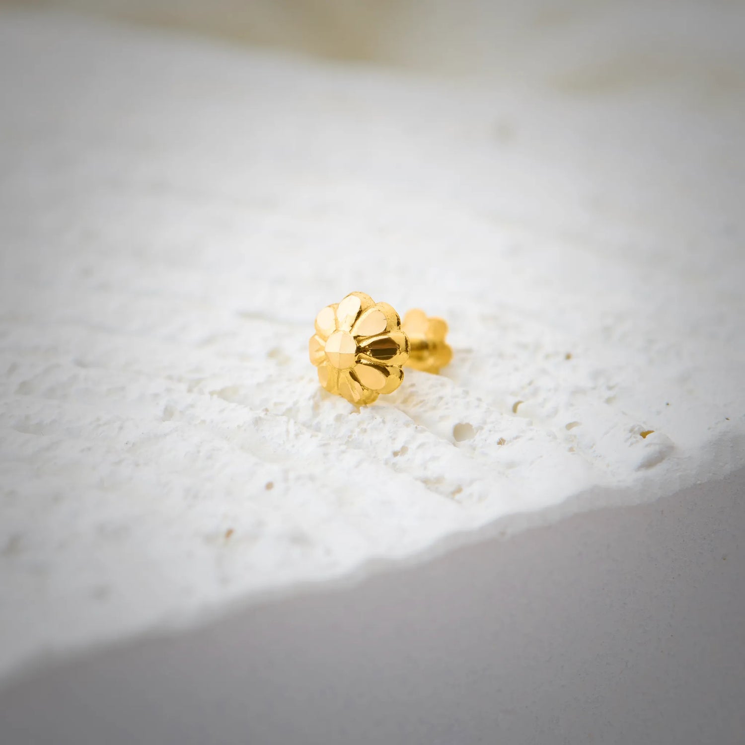 Gold floral nose pin photographed on a textured white surface showing its intricate detailing