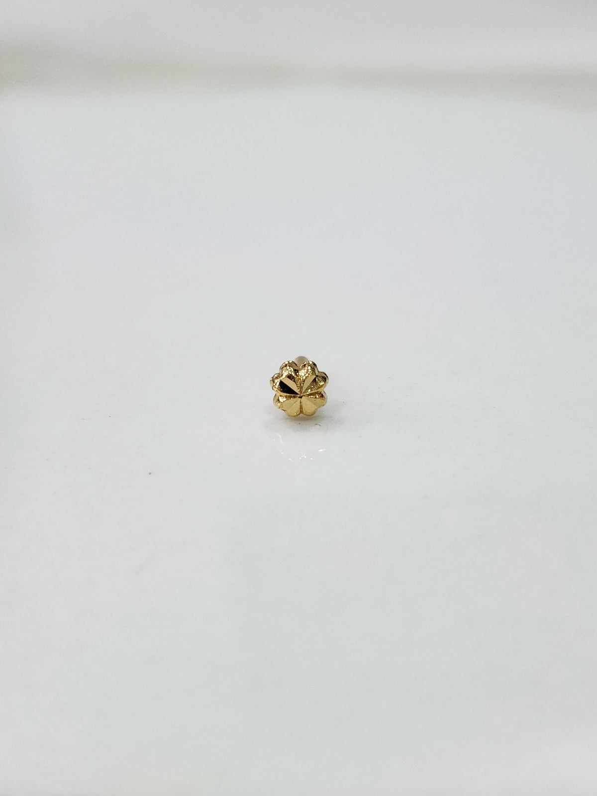 Side angled view of the small gold nose pin on a white surface highlighting its lightweight design