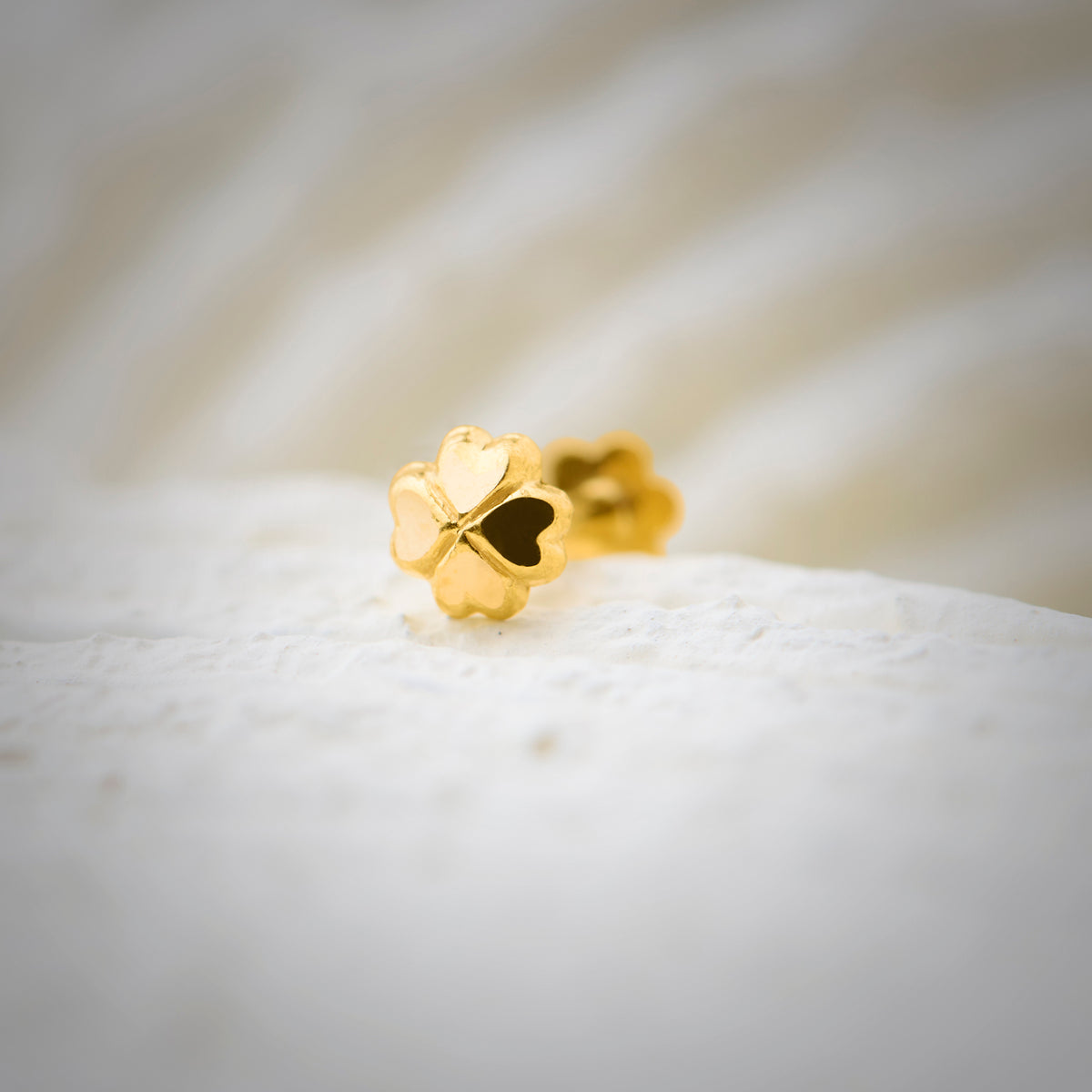Close up view of a polished gold nose pin placed on a white textured surface highlighting its smooth finish