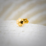Close up view of a polished gold nose pin placed on a white textured surface highlighting its smooth finish