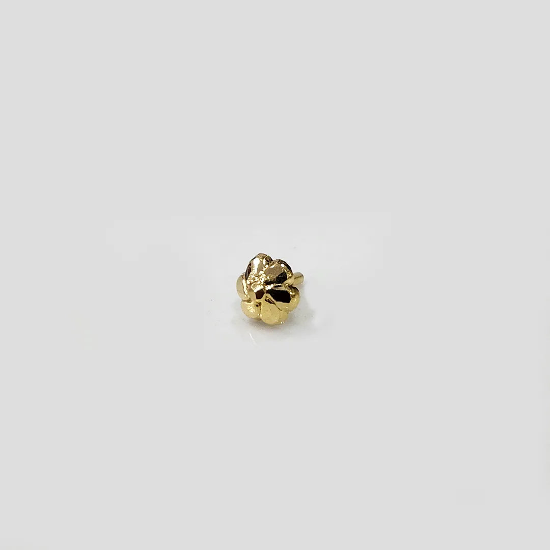 Top view of small floral gold nose pin on a light surface emphasizing minimal design